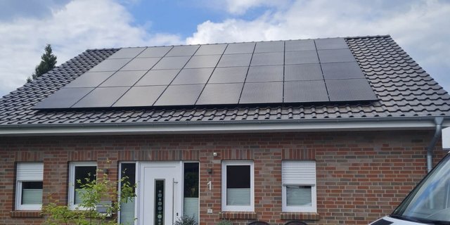 Ein modernes Haus mit einem schrägen Dach, das mit mehreren Solarpanelen bedeckt ist, unter einem klaren Himmel.