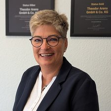 Die Frau trägt einen blauen Blazer und ein weißes Oberteil, während sie freundlich in die Kamera lächelt.