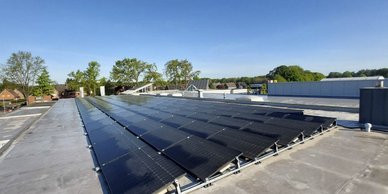 Die Solarpanels auf dem Dach reflektieren das Sonnenlicht, während Bäume und Häuser im Hintergrund sichtbar sind.