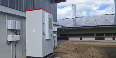 Im Vordergrund ist ein Wechselrichter zu sehen, während im Hintergrund die Solarpanels auf dem Dach glänzen.