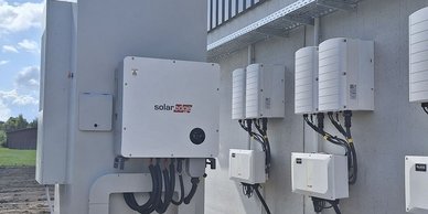 Die Installation von Solartechnologie zeigt mehrere Wechselrichter, die ordentlich an einer Wand angebracht sind, vor einer ländlichen Kulisse.